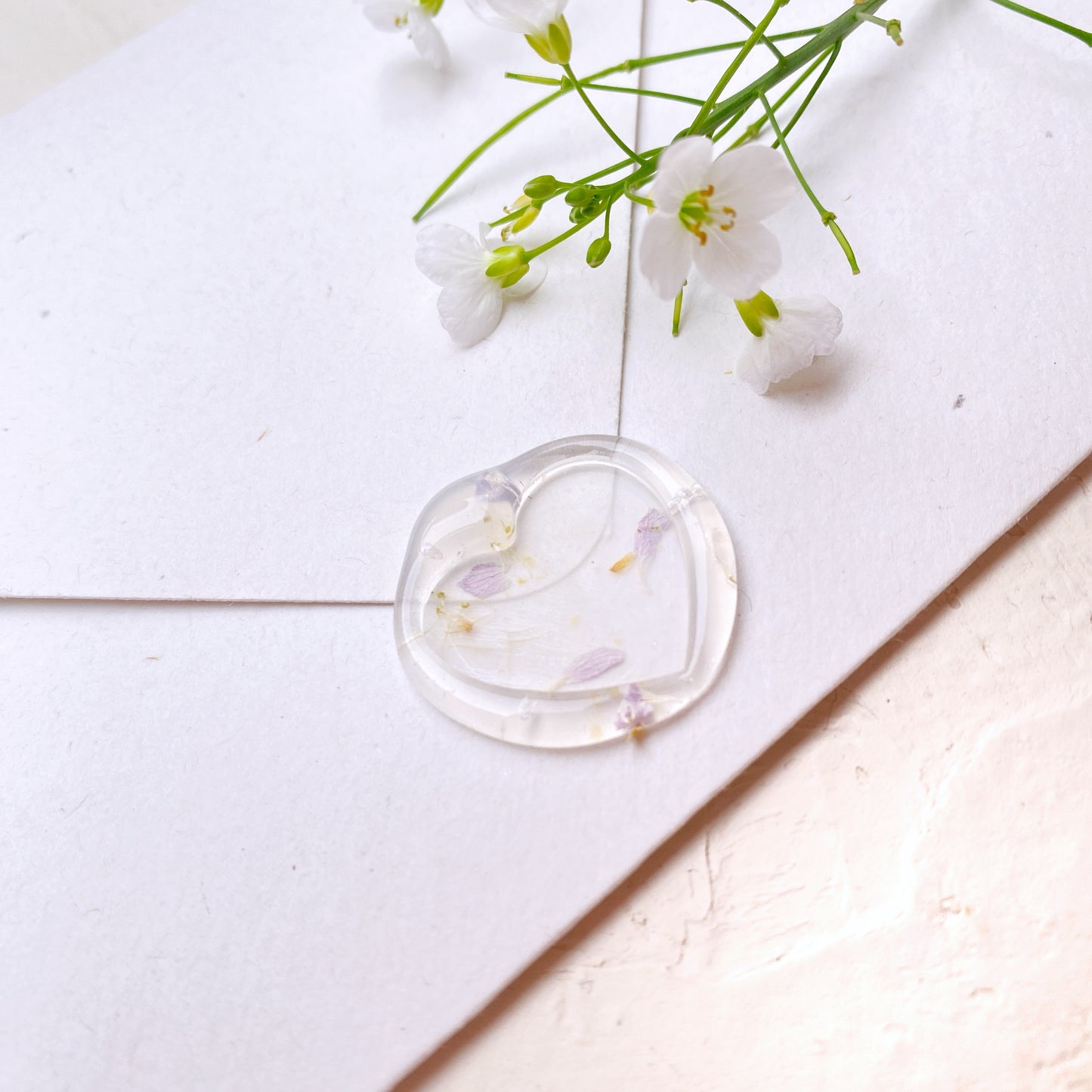 Průhledná pečeť srdíčko s květinami na svatební oznámení na přírodní obálce detail z profilu