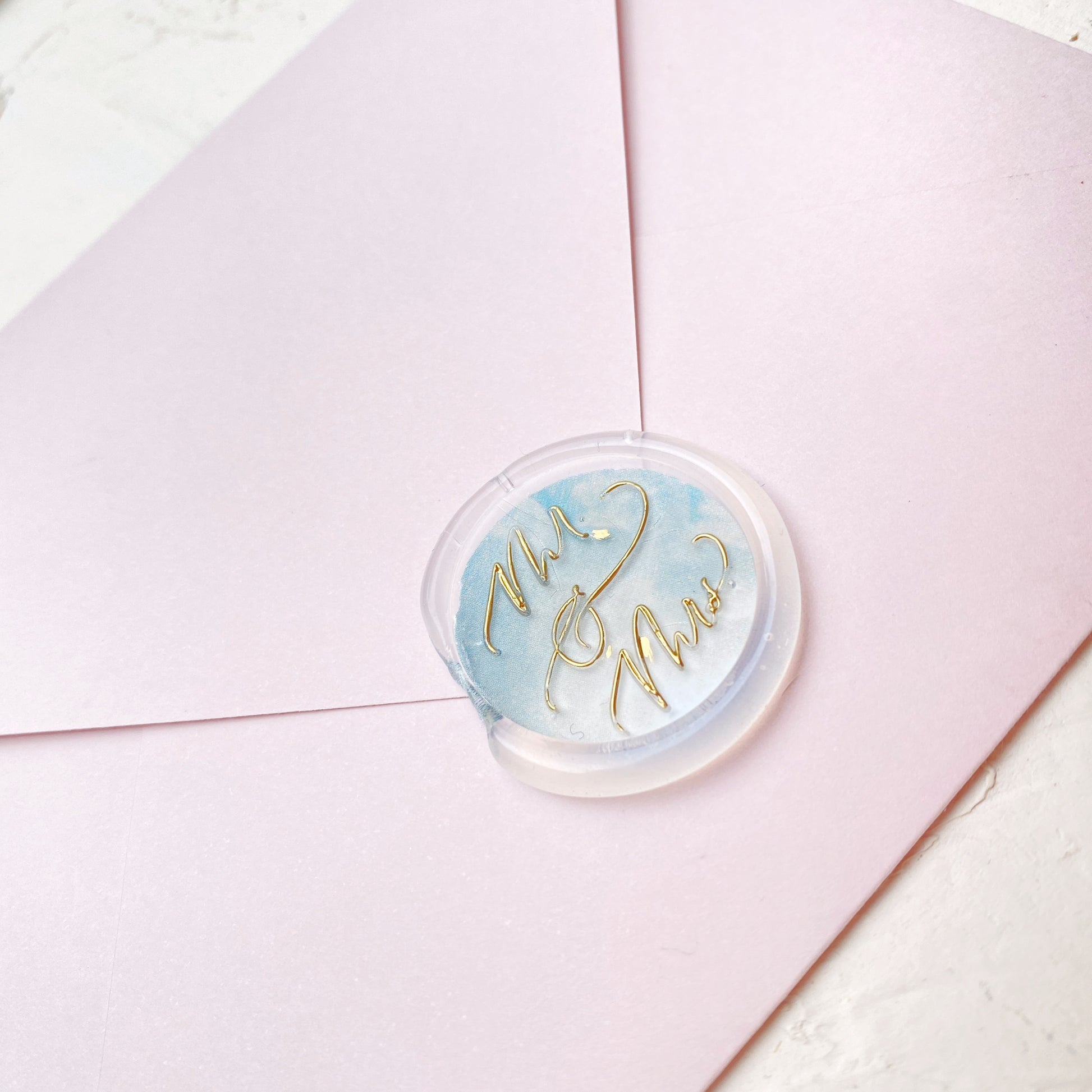 Hotová pečeť na svatební oznámení Mr. & Mrs. detail z profilu na růžové obálce se zlatým písmem