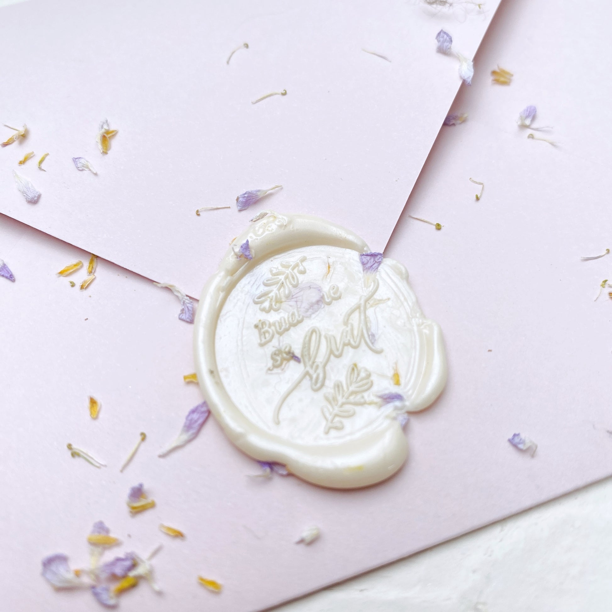 Bílá hotová pečeť "budeme se brát" na svatební oznámení na růžové obálce s květinami detail zeshora
