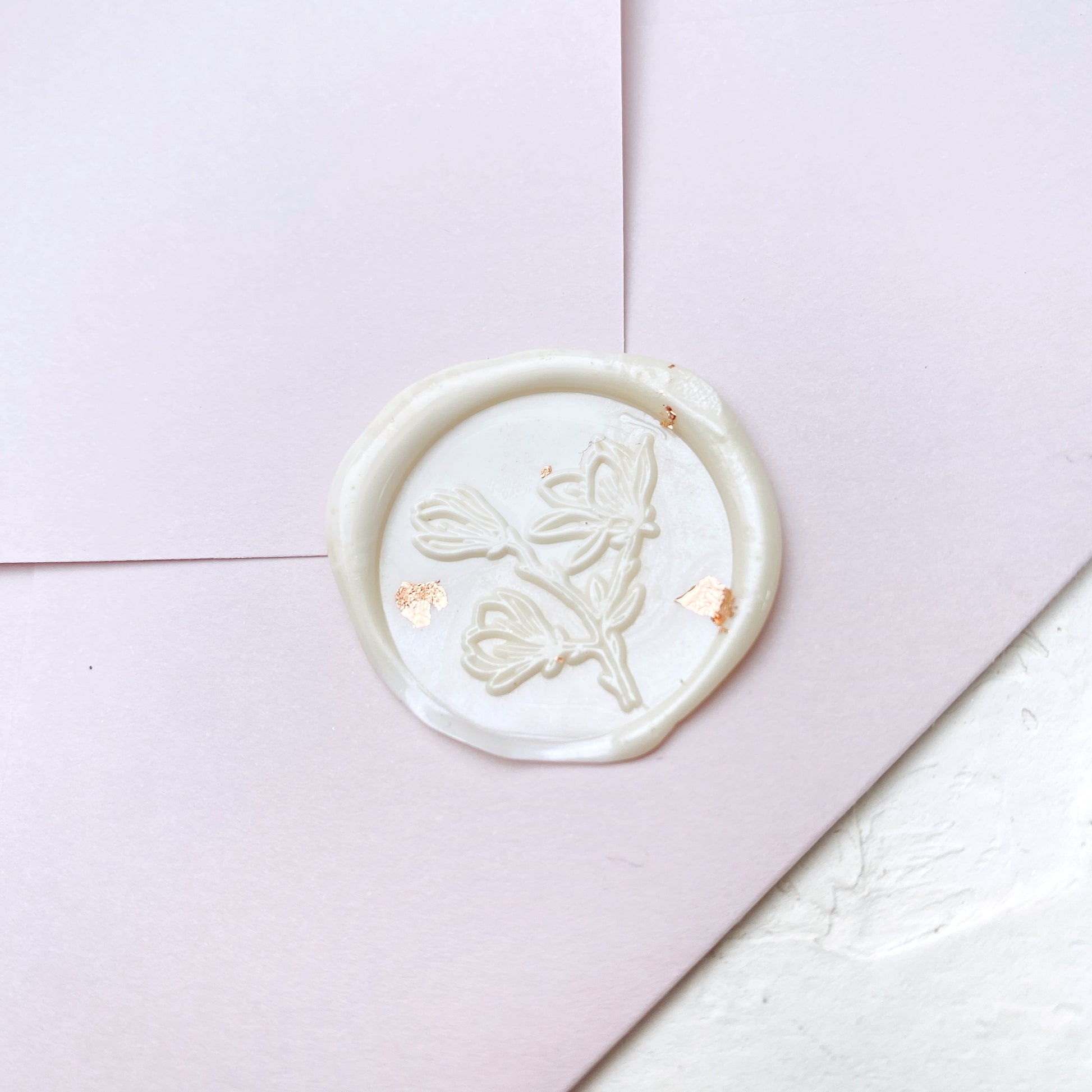 Krémová pečeť na svatební oznámení s motivem Magnolie a rose-gold dekorací na růžové obálce a bílém podkladu zeshora