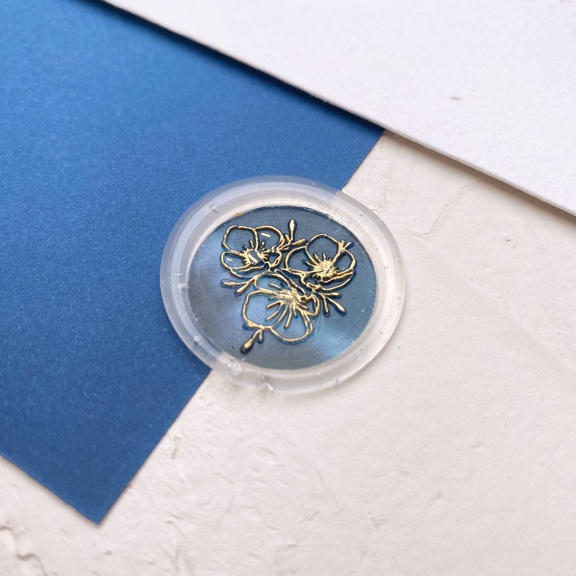 Průhledná pečeť s modrým výsekem a zlatým motivem květin na modro bílém podkladu zeshora
