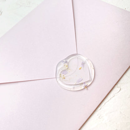 Průhledná pečeť ve tvaru srdce s květinami na růžové obálce a bílém podkladu z profilu